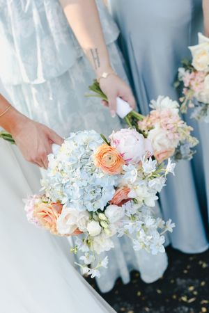 Row of bridesmaids holding elegant bouquets with light blue hydrangeas and peach ranunculus flowers.