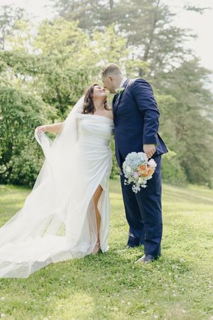 A bride and groom share romantic moments in a lush green field with flowing white dress and navy suit.