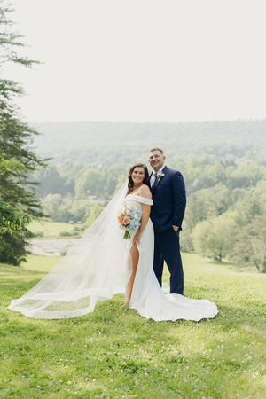 Newlywed couple poses on a scenic hillside overlooking a lush green valley on their wedding day.