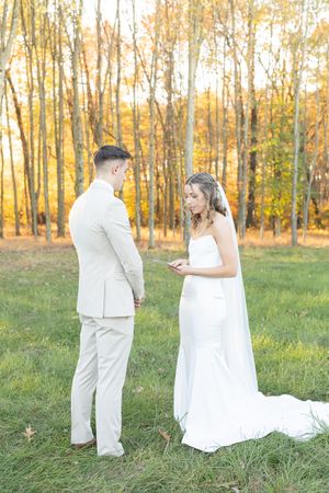 A couple exchanging vows in an autumn forest setting with golden light filtering through birch trees.