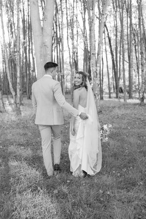 Black and white wedding photos of couple walking through serene birch forest.