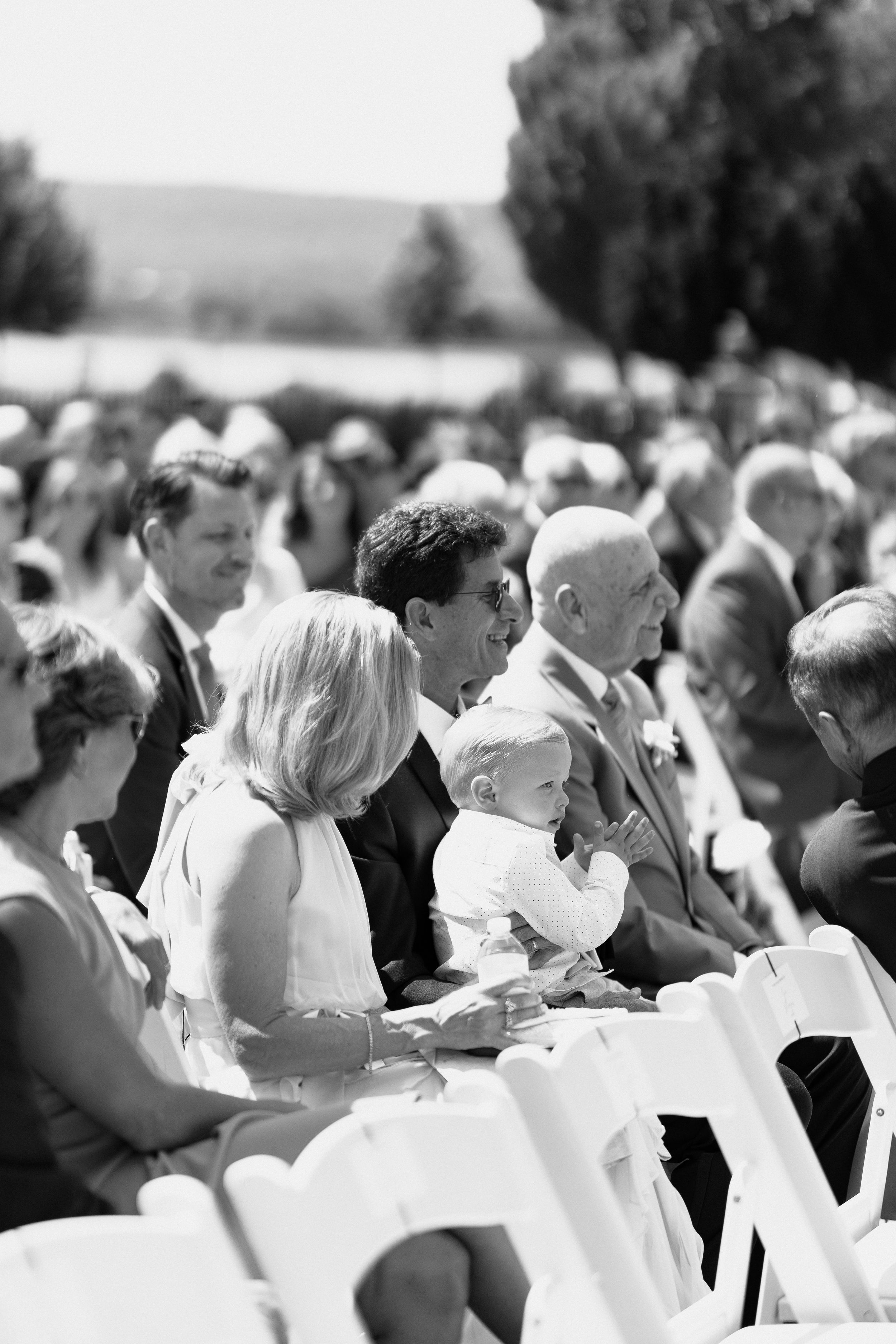 Black and white photo of outdoor wedding ceremony audience seated in rows.