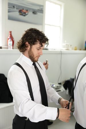 A person in a white dress shirt and black suspenders adjusts their attire while getting ready.