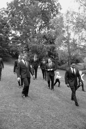 A sequence of black and white photos showing groomsmen walking in formation across a grassy field.
