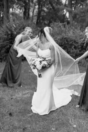 Black and white photo of a flowing wedding dress and veil being captured in motion against a natural outdoor backdrop.