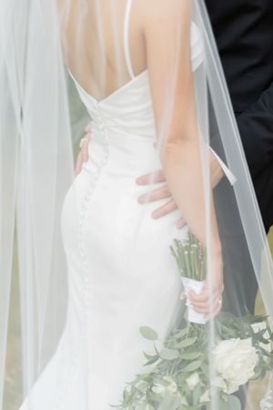 A close-up view of a white wedding dress and flowing veil against a dark background.