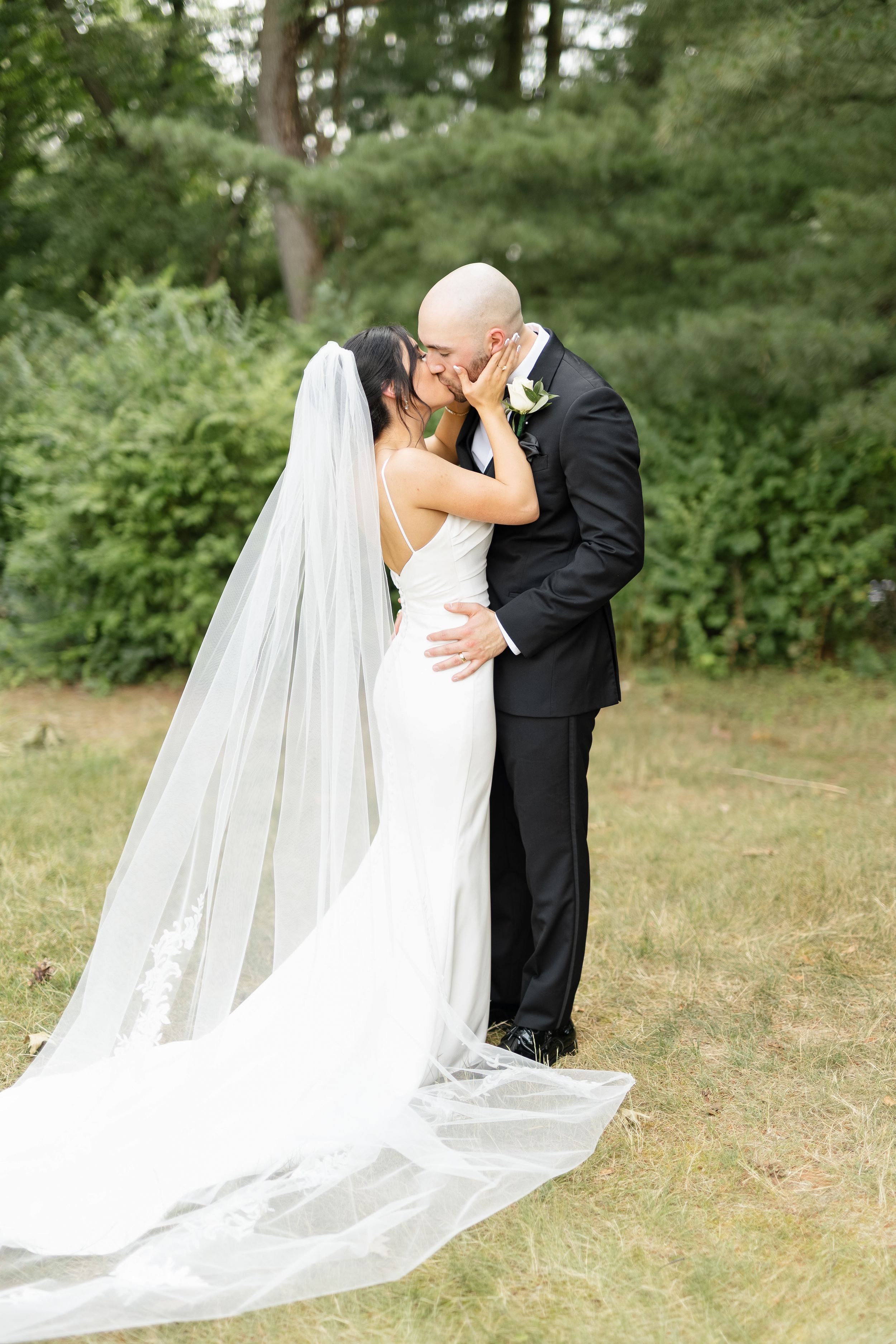 A romantic wedding moment captured outdoors with a flowing white veil against a natural backdrop.