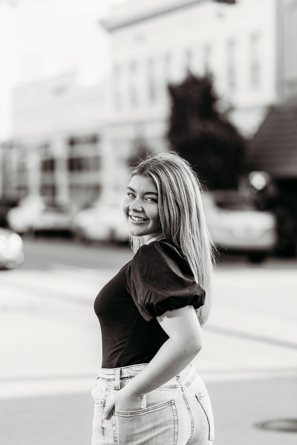 Black and white portrait of student in casual attire posing on city street.