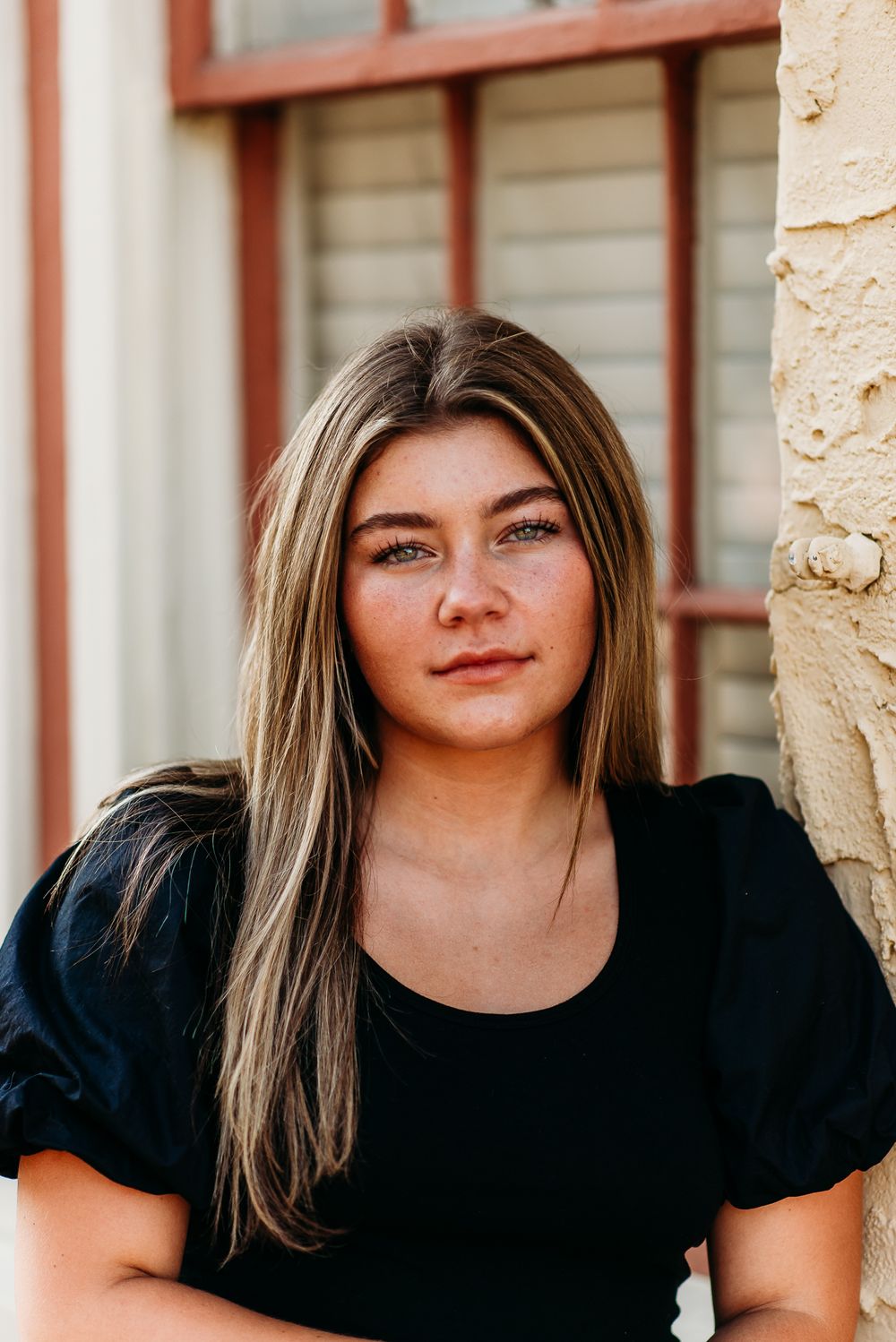 Portrait shot of a woman wearing a black puff-sleeve top against a stone wall.