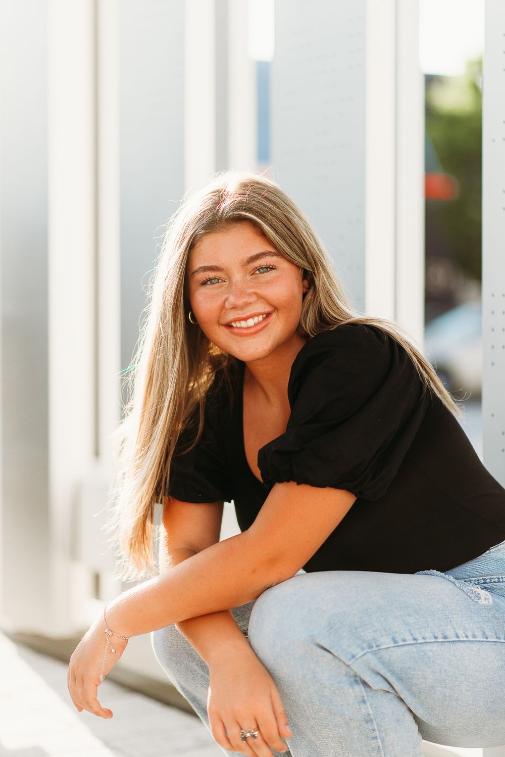 Casual portrait of a woman in black top and jeans sitting outdoors with a bright smile.