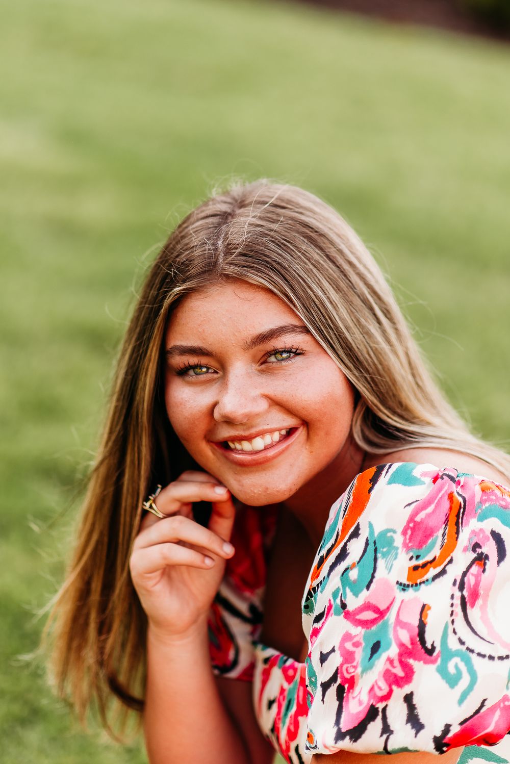 Woman in floral dress poses on grass with natural lighting.