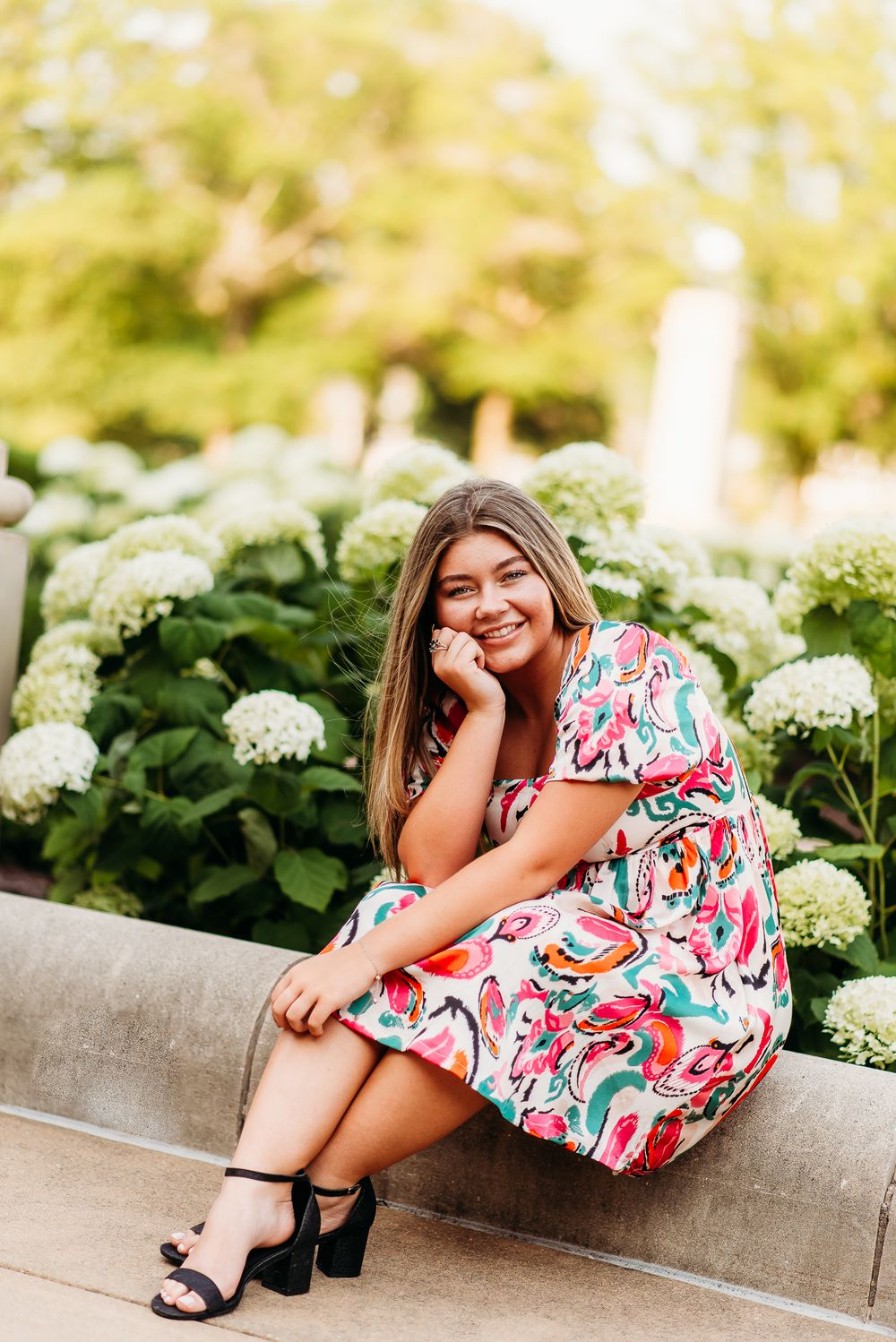 Outdoor portrait with hydrangea bushes of woman in patterned dress.