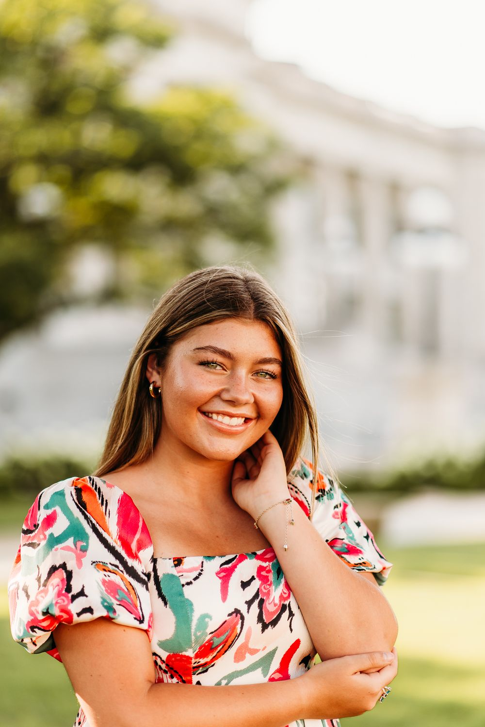 Outdoor summer portrait of woman in colorful floral dress against blurred building background.