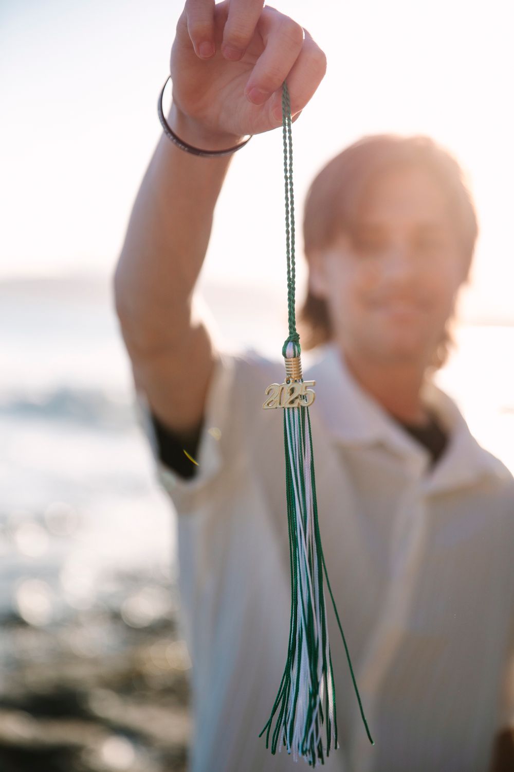 Someone holding up a graduation tassel with '2023' charm against a sunlit outdoor background.