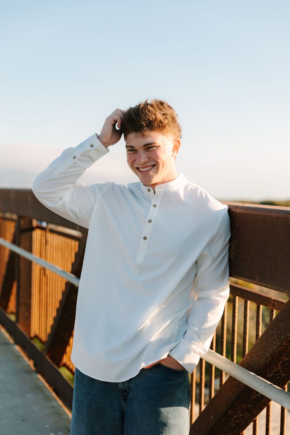 Someone in white shirt leaning on wooden railing during golden hour by the beach.