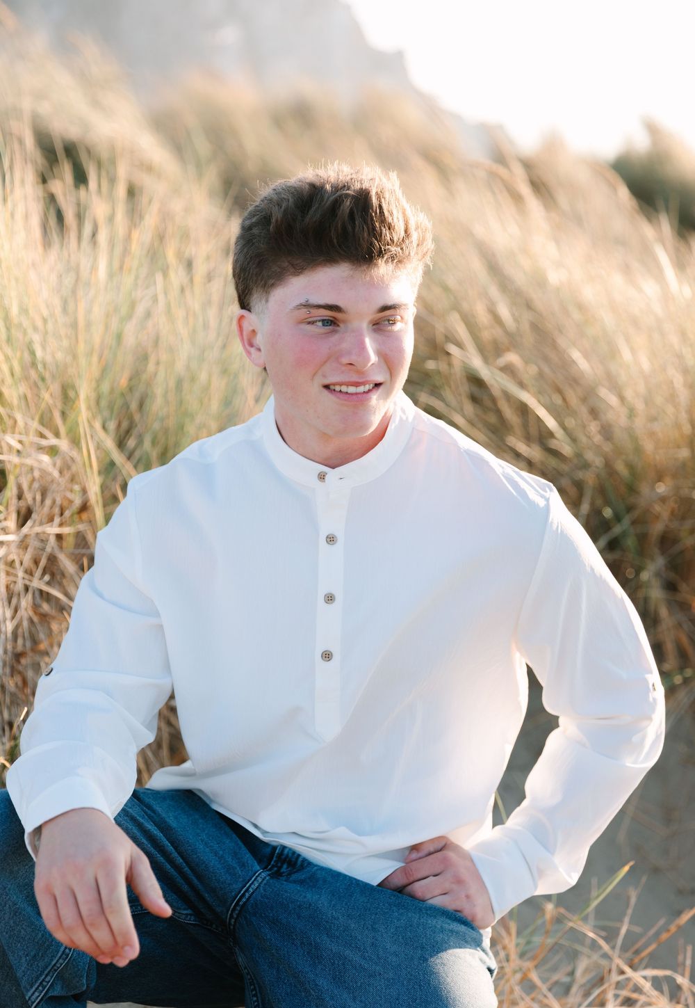 A series of portraits showing someone sitting in tall grass wearing blue jeans and a white henley shirt at sunset.