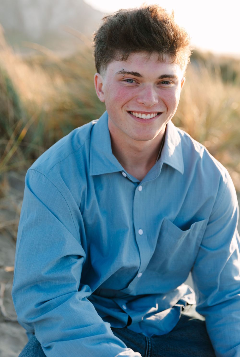 Portrait series of someone in a light blue button-down shirt sitting in a field during golden hour.