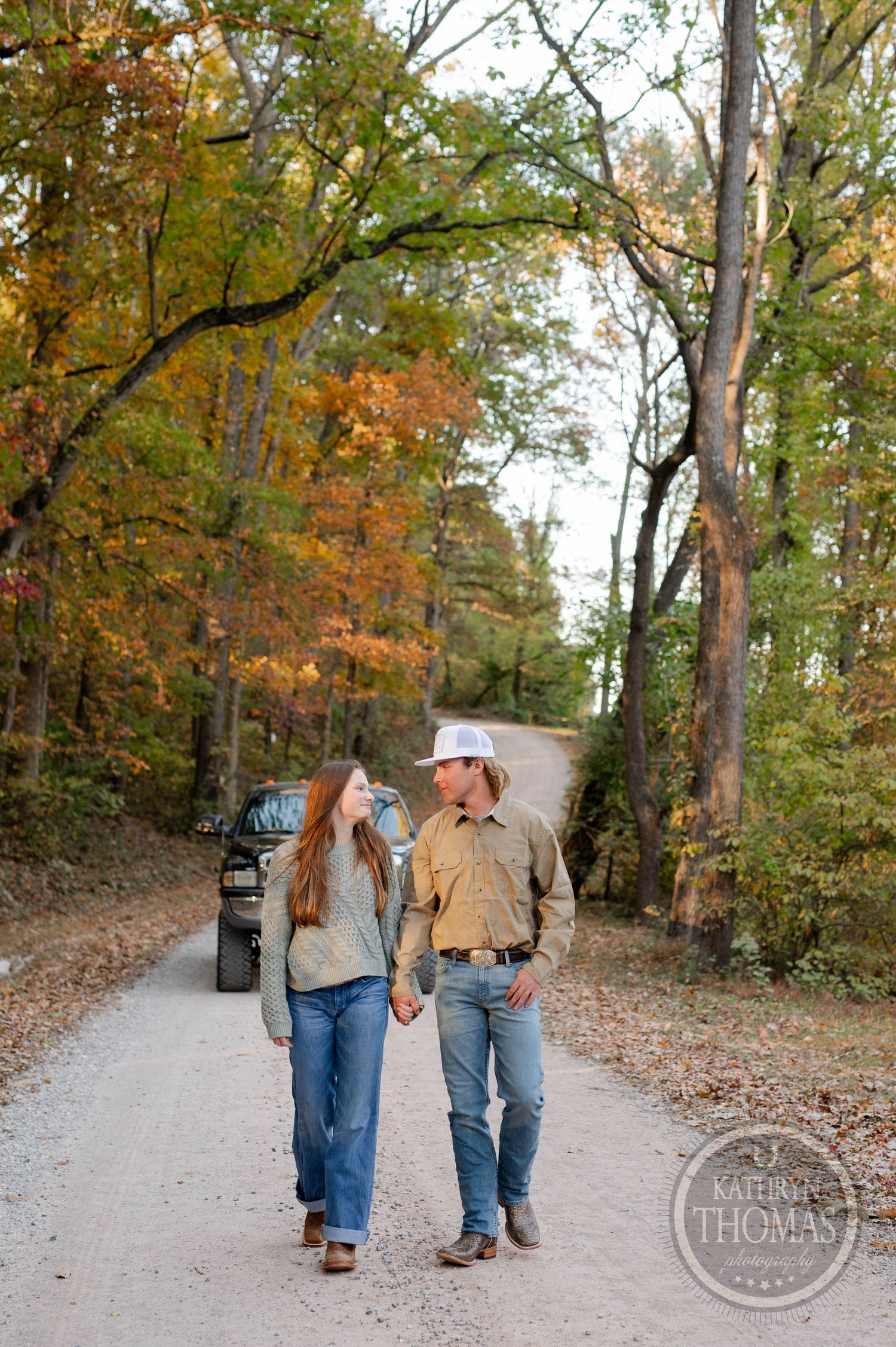 A couple takes a romantic stroll down a leaf-covered forest path during autumn.