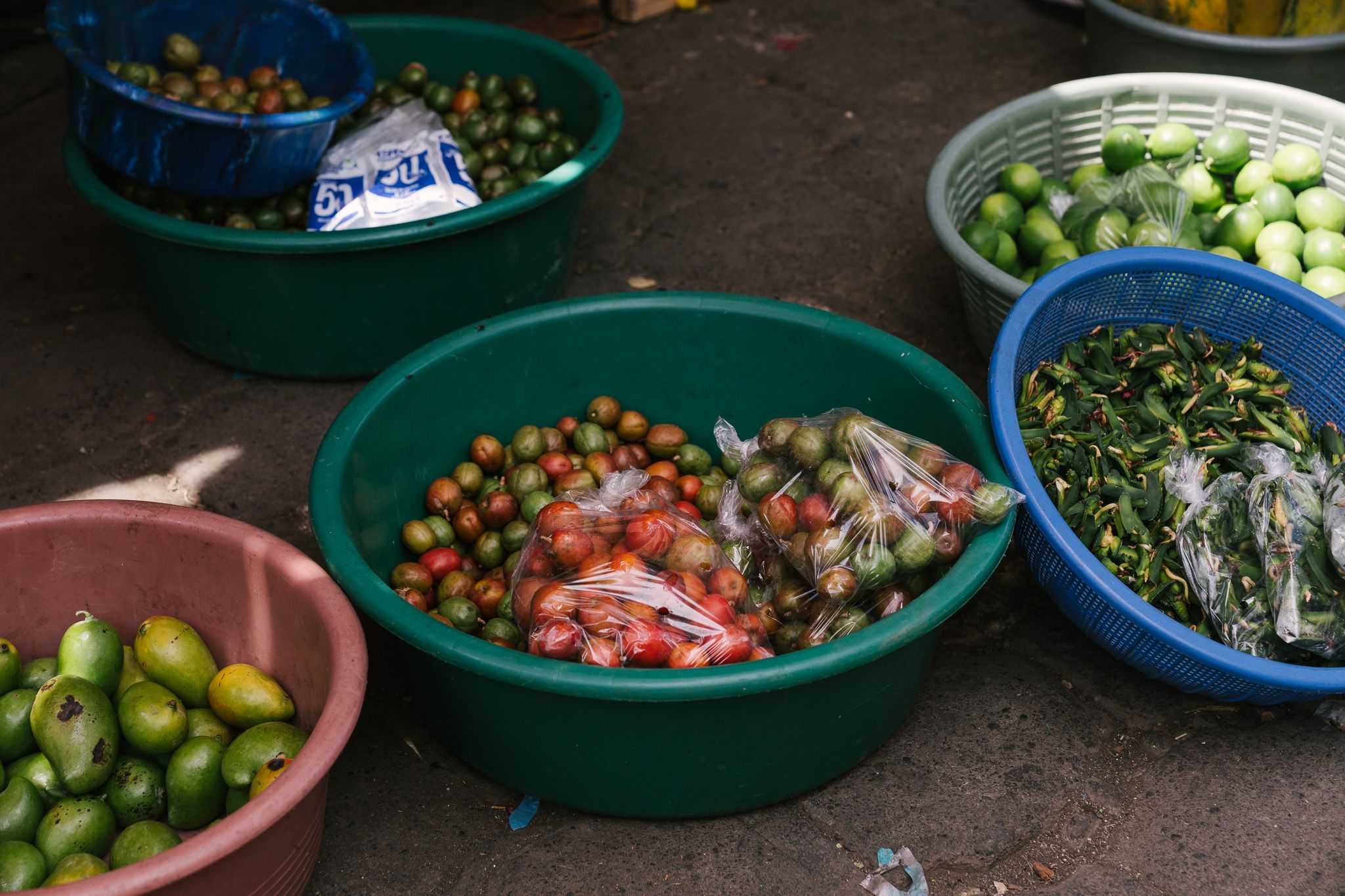 Fresh produce and ingredients displayed in colorful plastic bowls at market.
