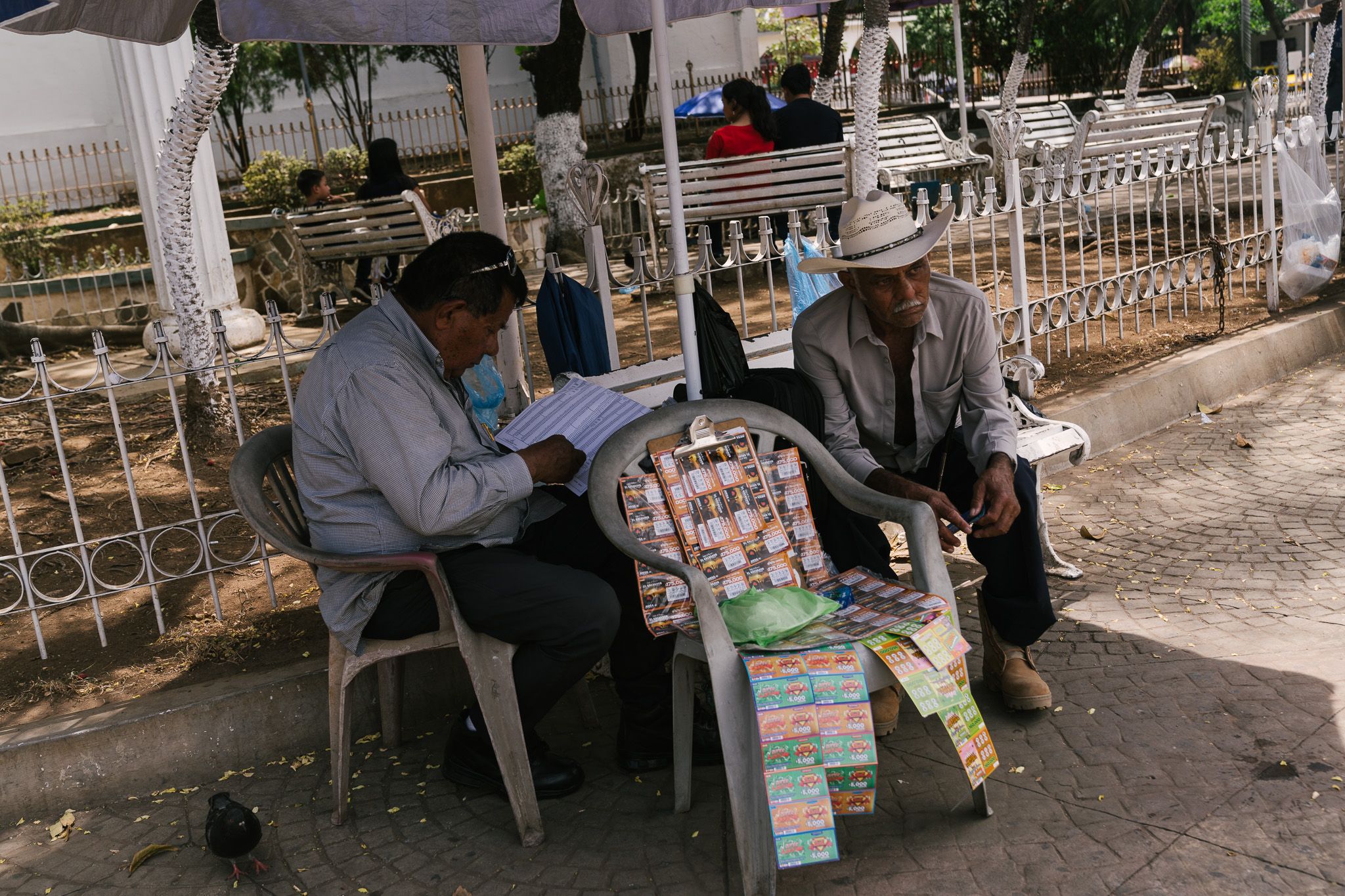 Street vendors selling lottery tickets and candies while sitting on plastic chairs.
