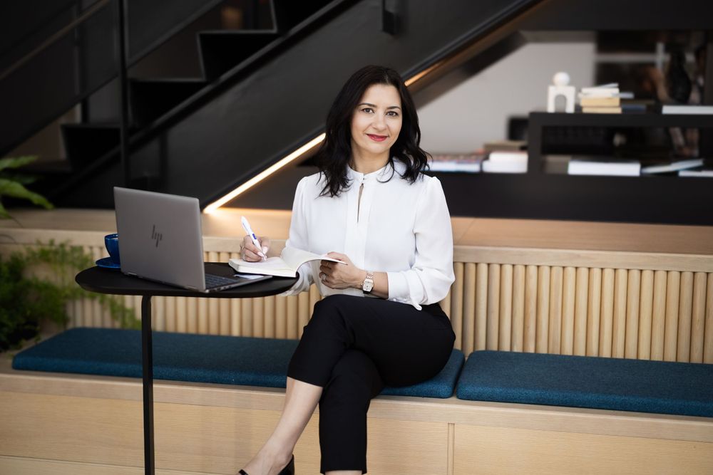 Professional woman in white blouse sitting with laptop in modern office space.