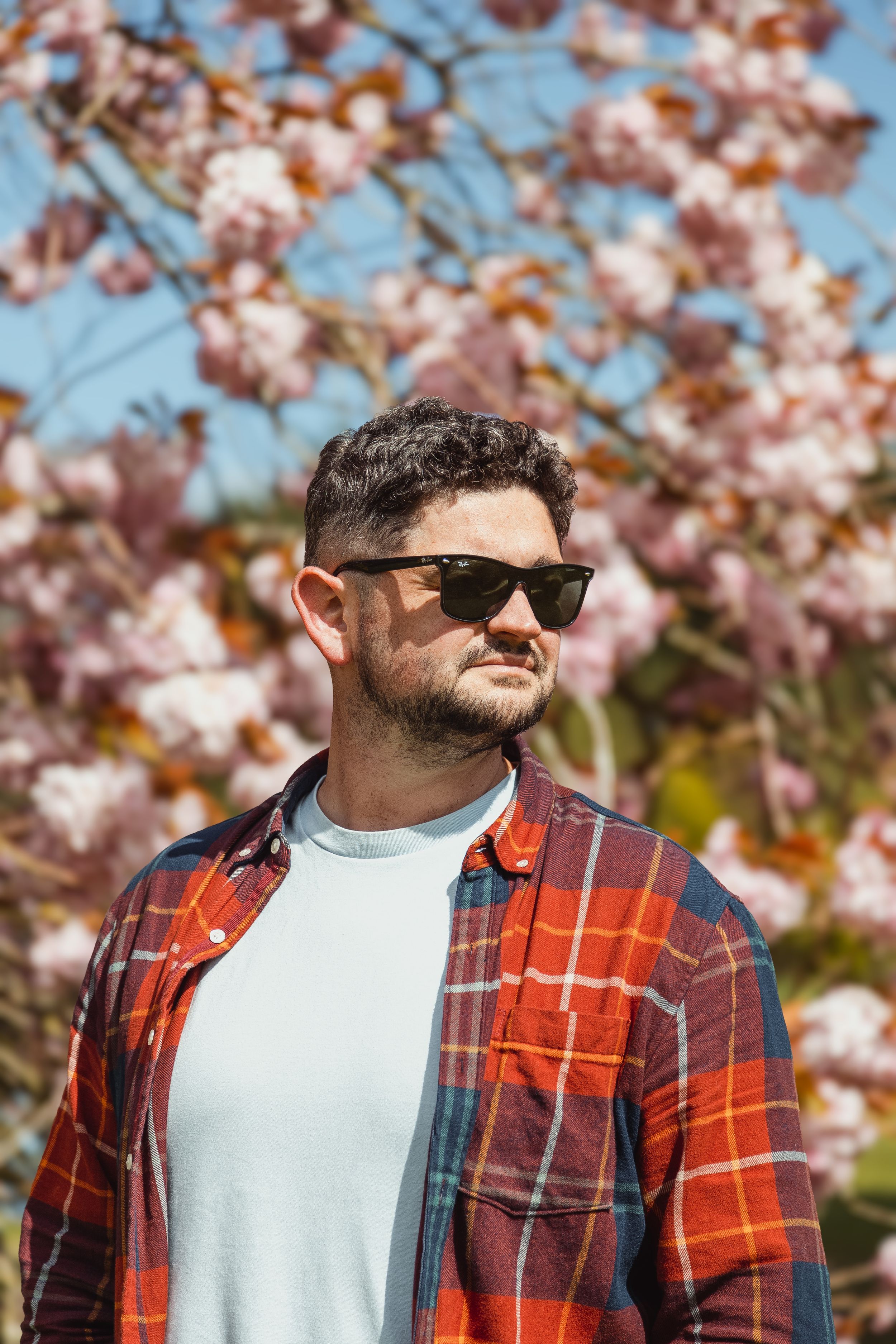 Spring portrait with cherry blossoms and red plaid shirt against blue sky.