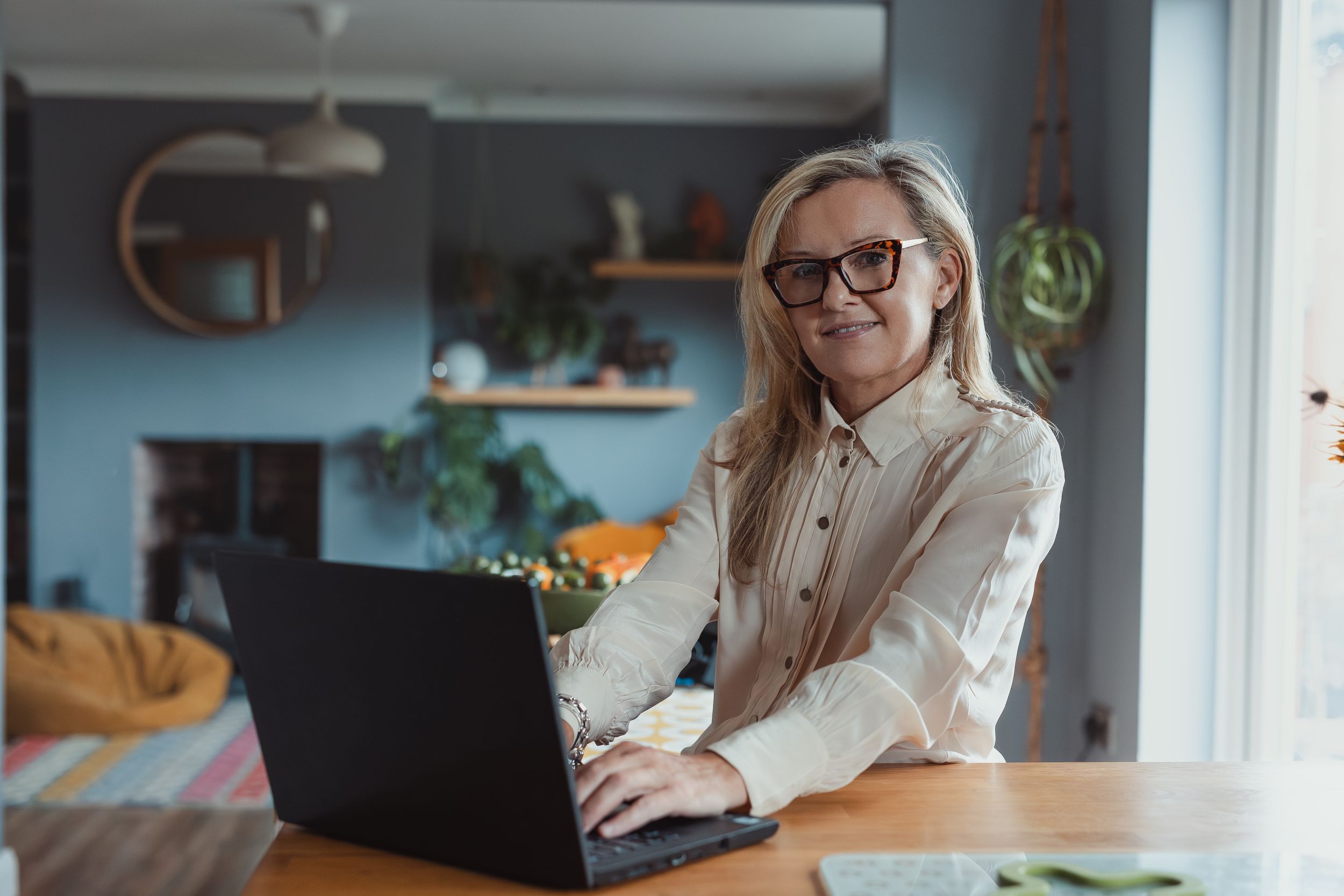 Person in glasses working on laptop in home office with natural lighting and blue walls.