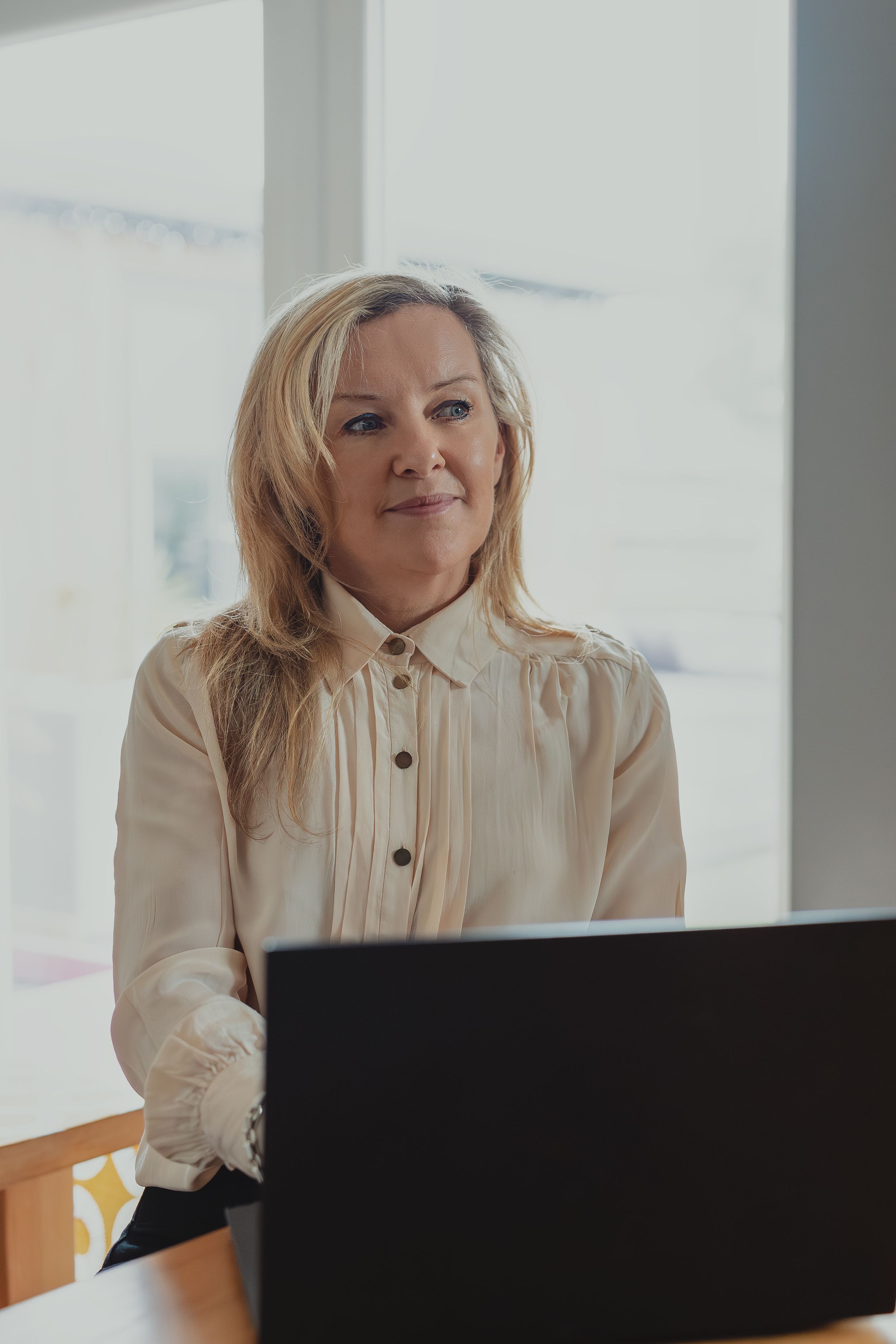 Professional working at a desk in a bright modern office space wearing a cream colored button-up blouse.