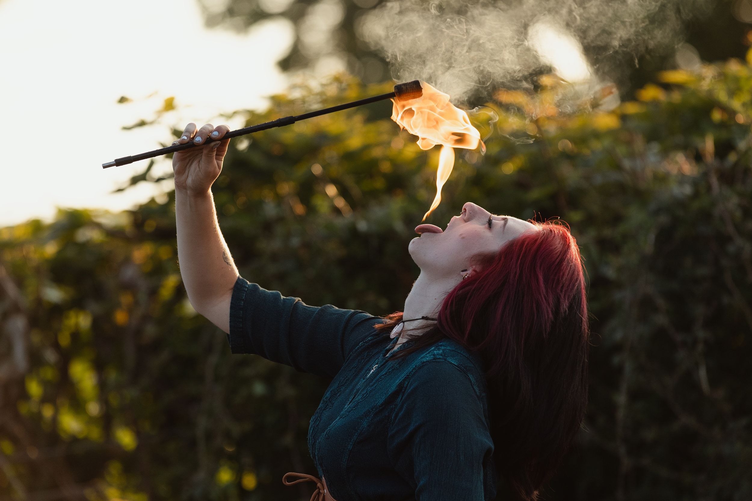 Fire performer spinning flames against dark evening sky creating light trails.