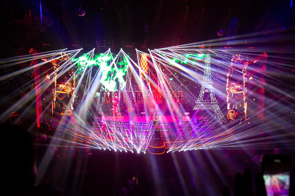 Colorful laser light beams create dynamic patterns across a dark stage during a concert performance.