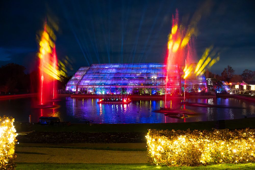 Glow at RHS Wisley with colourful illuminated glasshouse with vibrant red and blue glowing fountains.