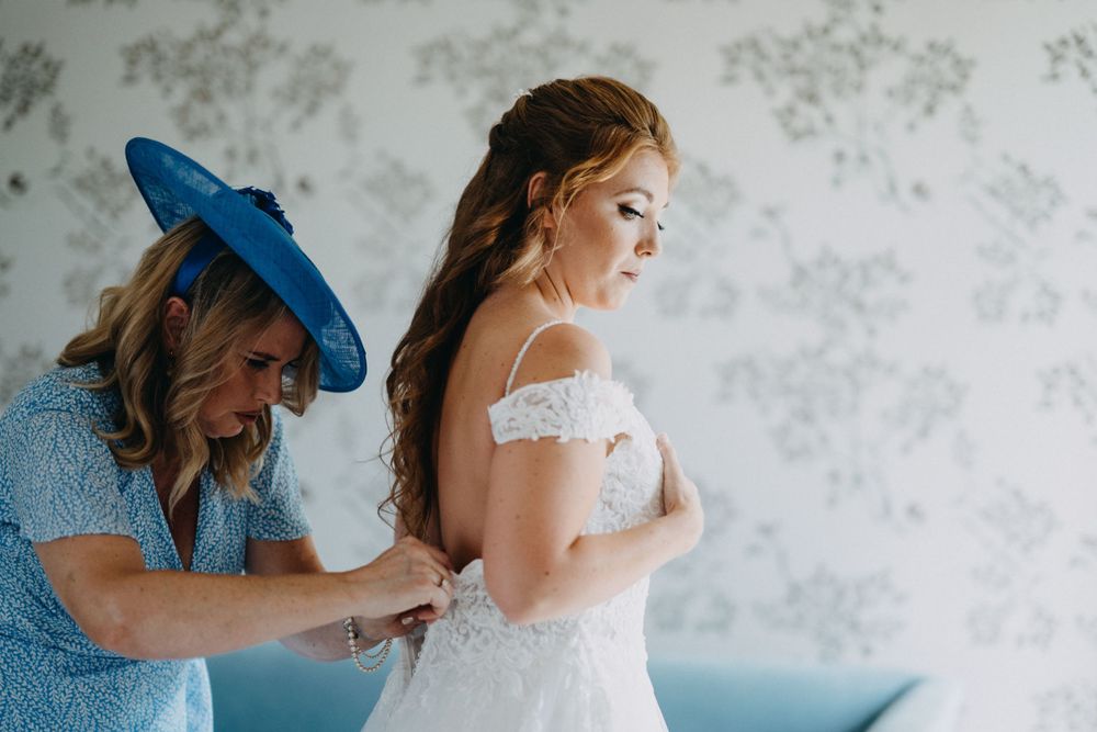 Helpers assisting with the final touches of a white lace wedding dress.