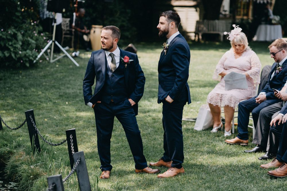 Wedding guests in formal attire stand on grass during an outdoor ceremony.