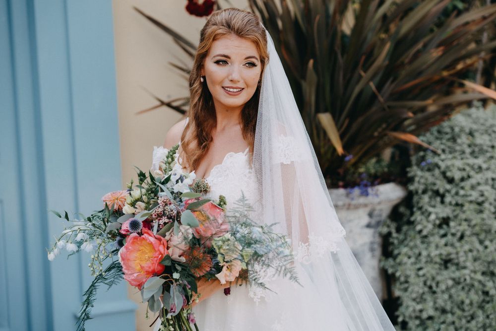 Bridal portrait with coral and peach bouquet against blue wall and tropical plants.