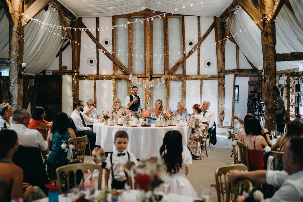 Wedding reception in progress inside rustic barn at South Farm with exposed beams and string lights.