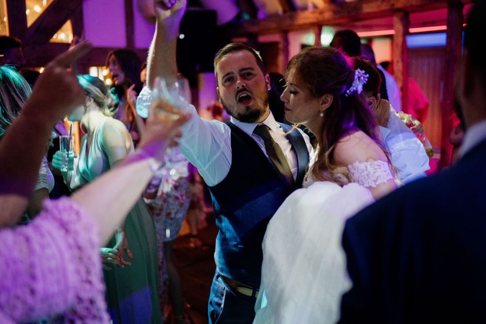 Wedding guests dance and celebrate on a colorfully lit dance floor during an evening reception.
