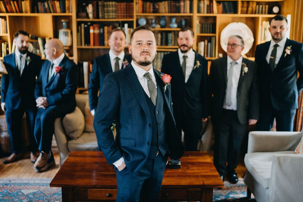 Groom and groomsmen in navy suits pose in an elegant library setting.