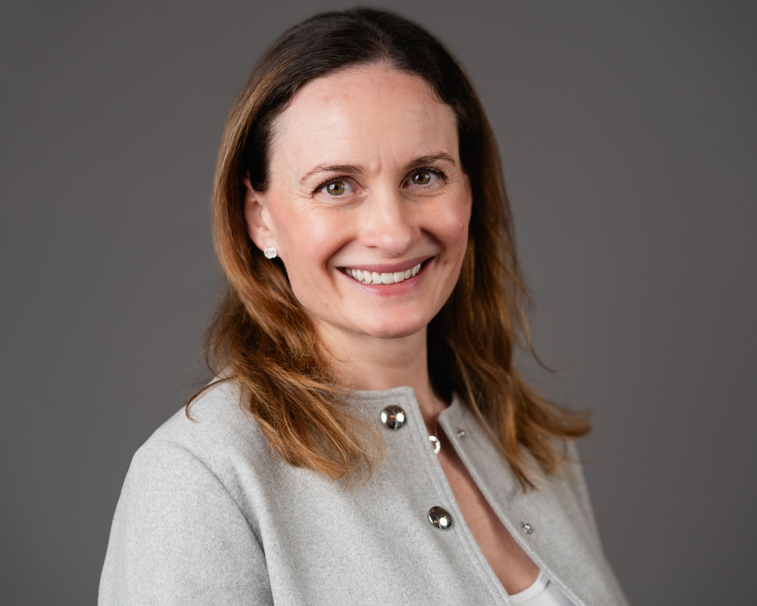 Professional headshot of someone in a light gray cardigan sweater smiling against a gray background.