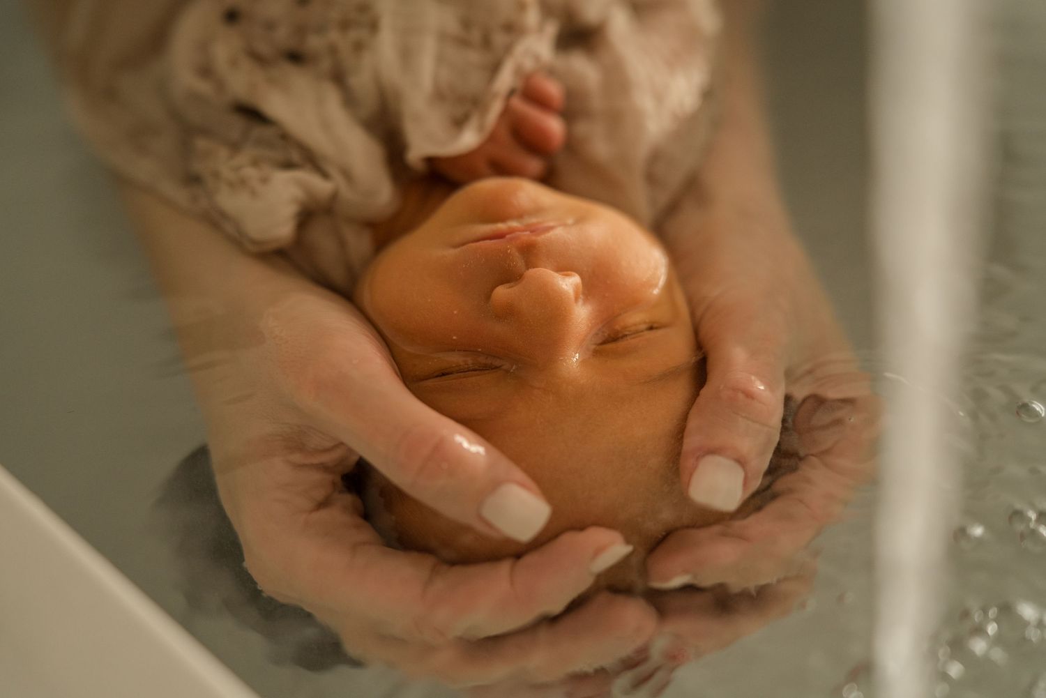 photo lors d'un thérapeutique bain bébé, le bébé et dans l'eau et les mains de l'accompagnante périnatal enveloppe sa tête