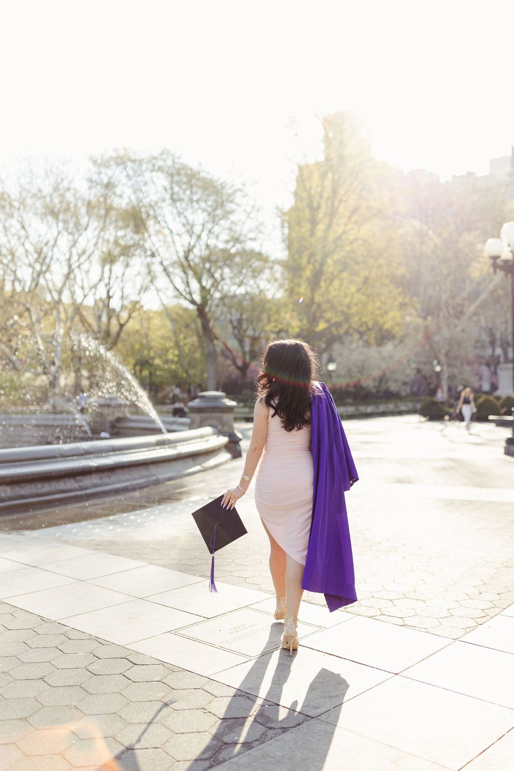 Graduate walking with purple regalia and diploma holder in golden afternoon light.