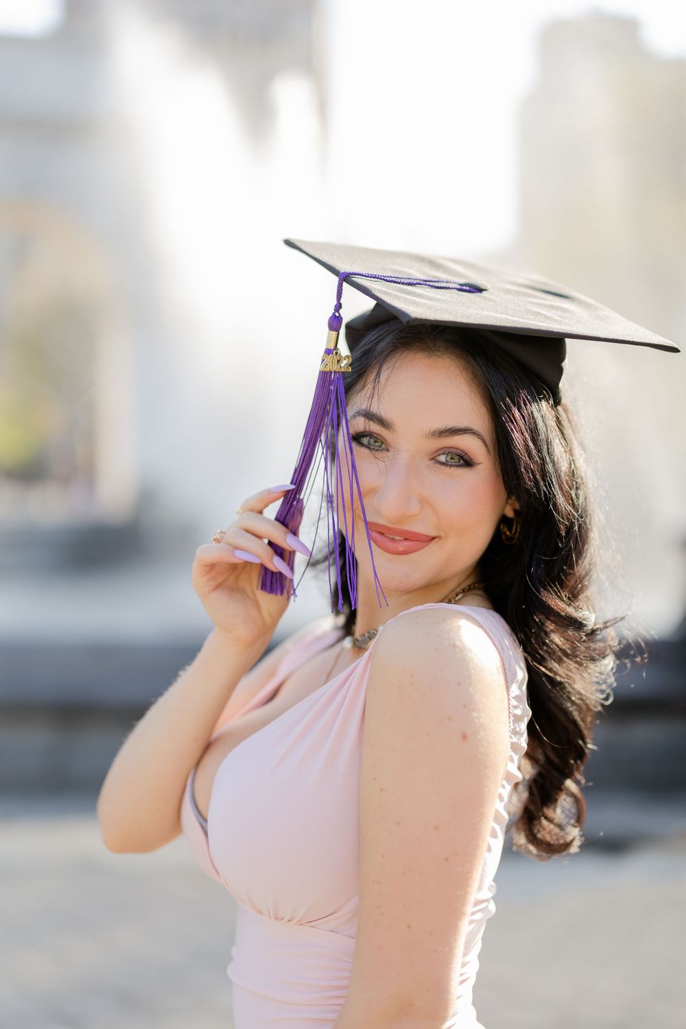 Graduate in pink dress wears cap with purple and gold tassel.