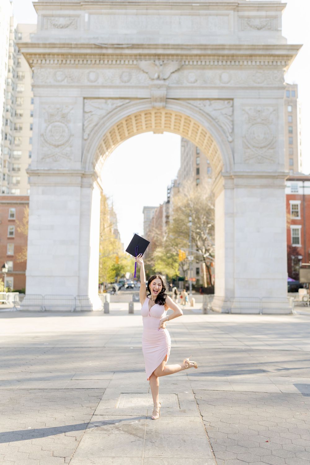 Graduate celebrating by jumping and tossing cap in front of iconic stone arch.