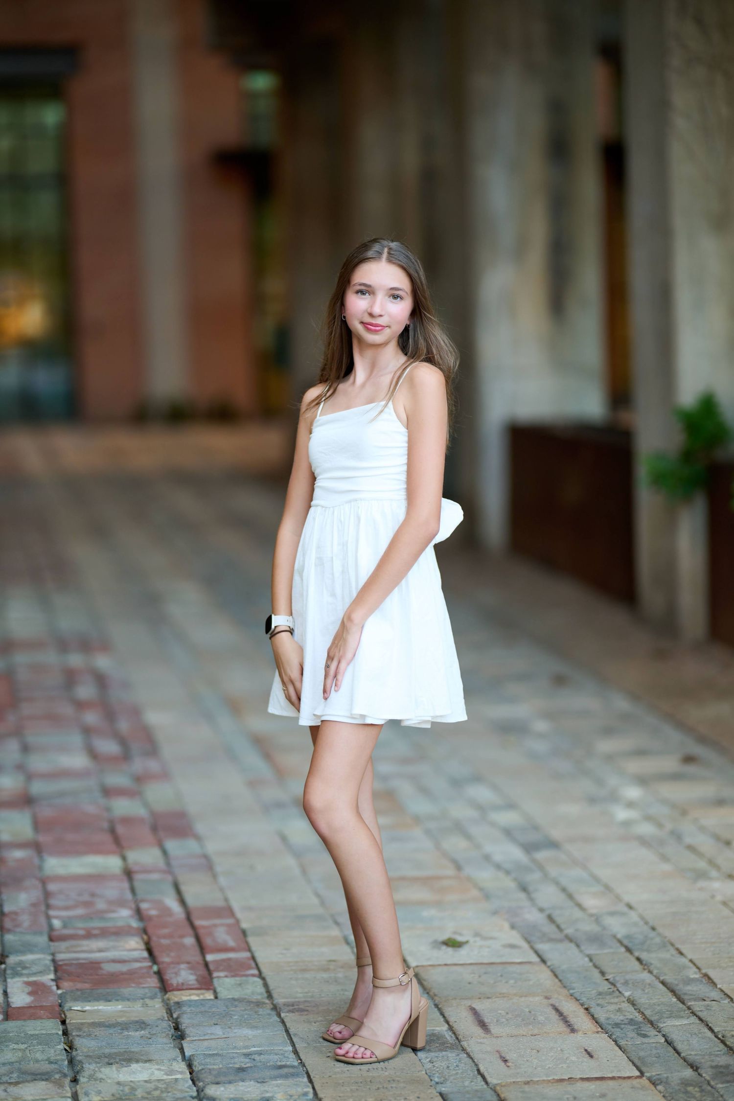A person in a white summer dress and heels poses outdoors on a brick pathway.