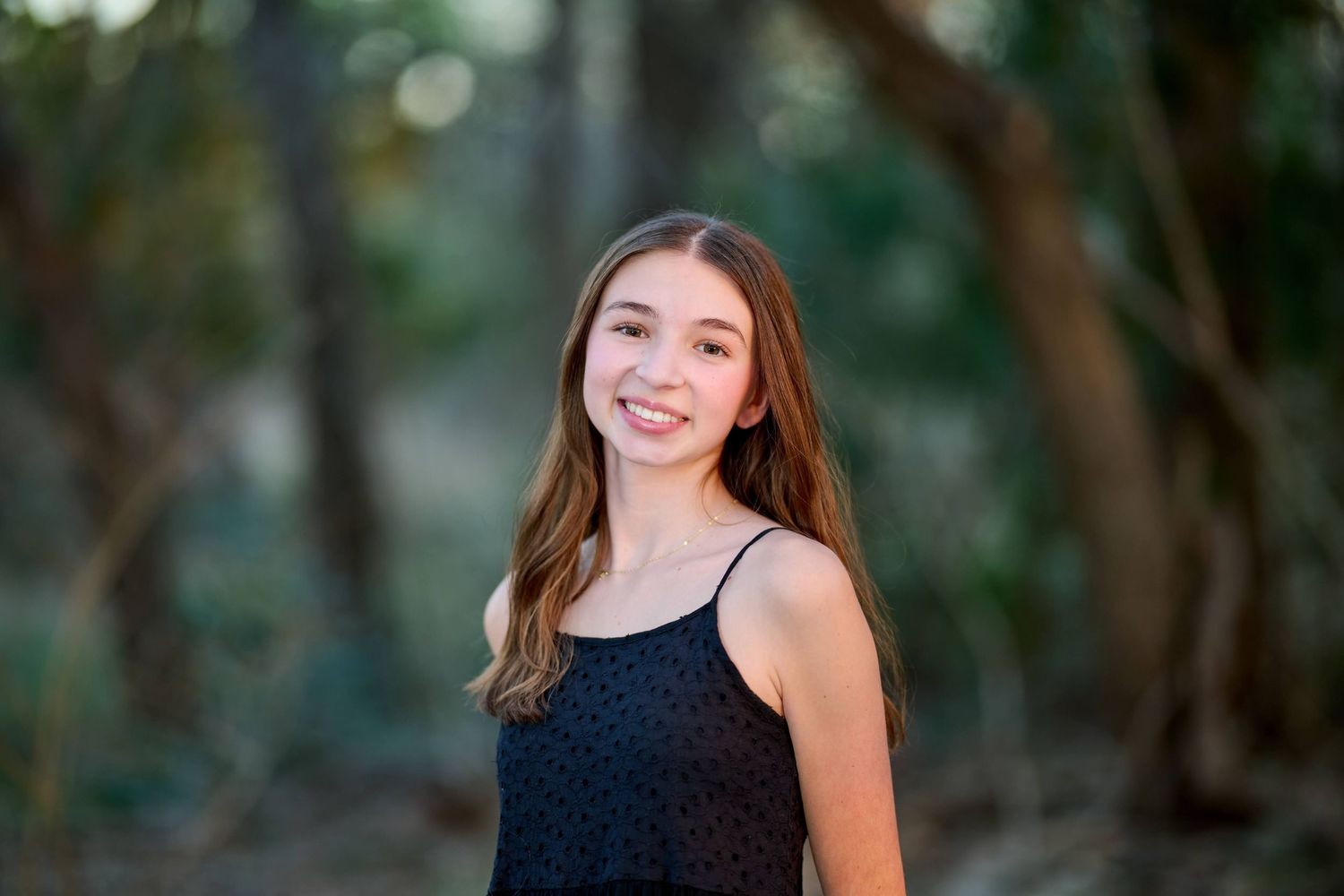 A portrait of a smiling person in a dark sleeveless top against a blurred natural background.