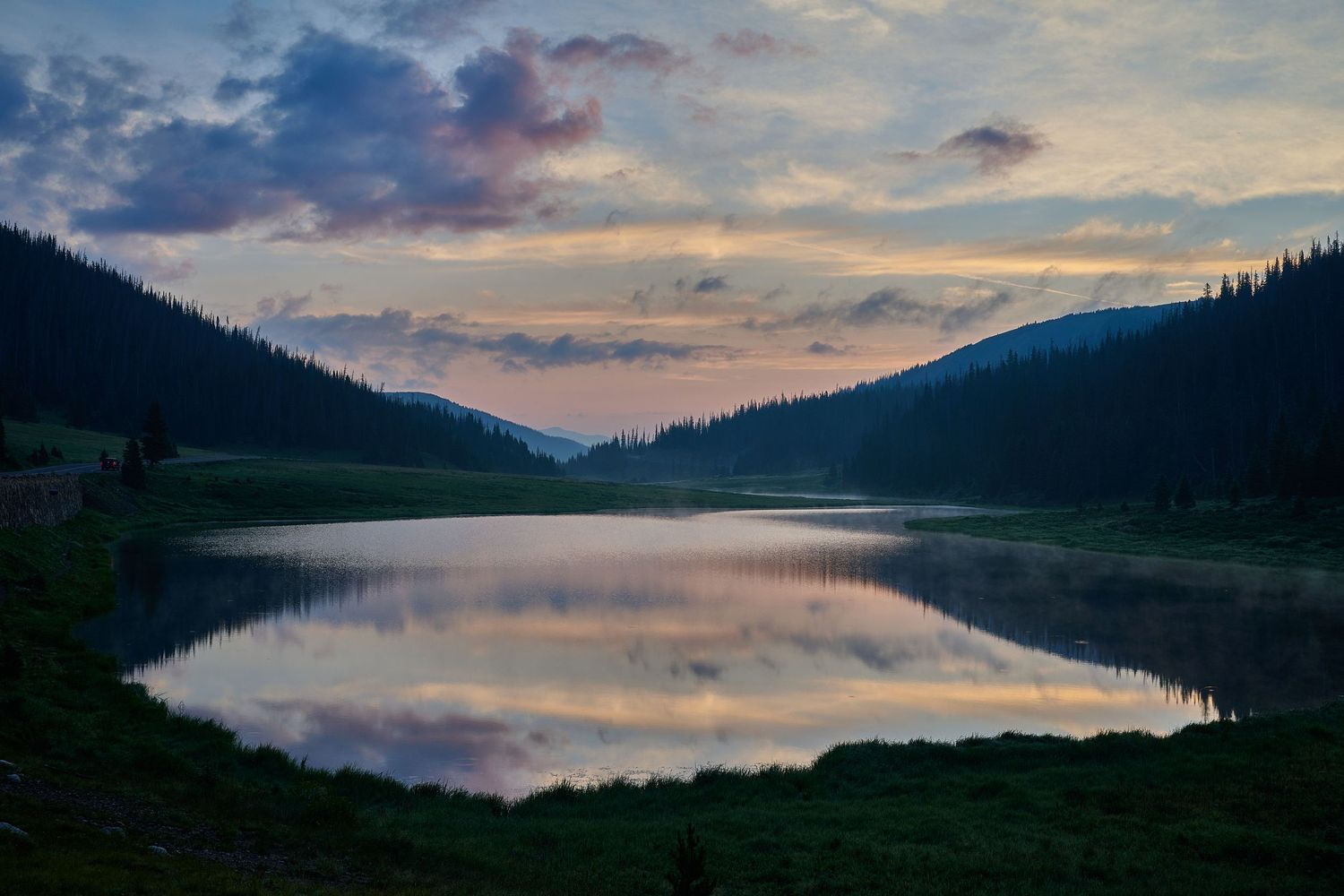 Panoramic view of a serene lake at sunset with mountains reflecting in the calm water.