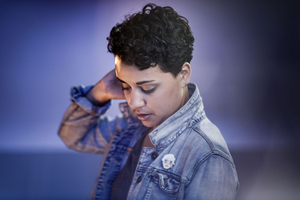 Person in denim jacket looking down thoughtfully against blue background lighting.