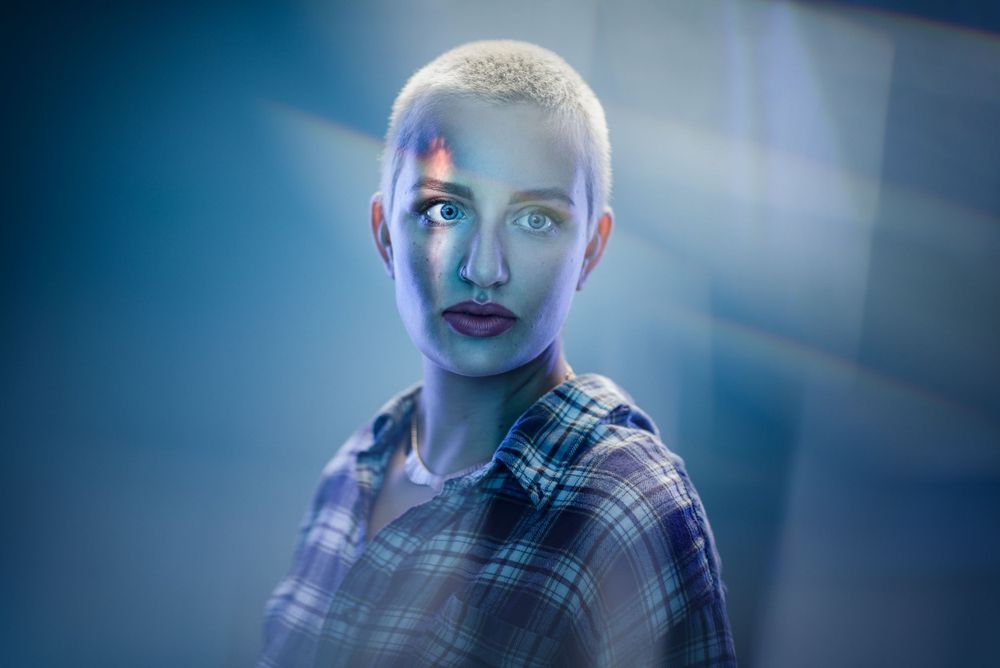 Close-up portrait with blue lighting showing person in plaid shirt with short blonde hair.