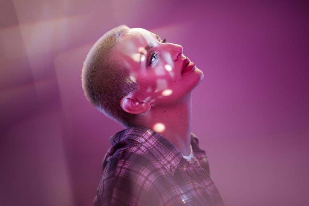 Artistic portrait in pink lighting showing person with short hair tilting head back.