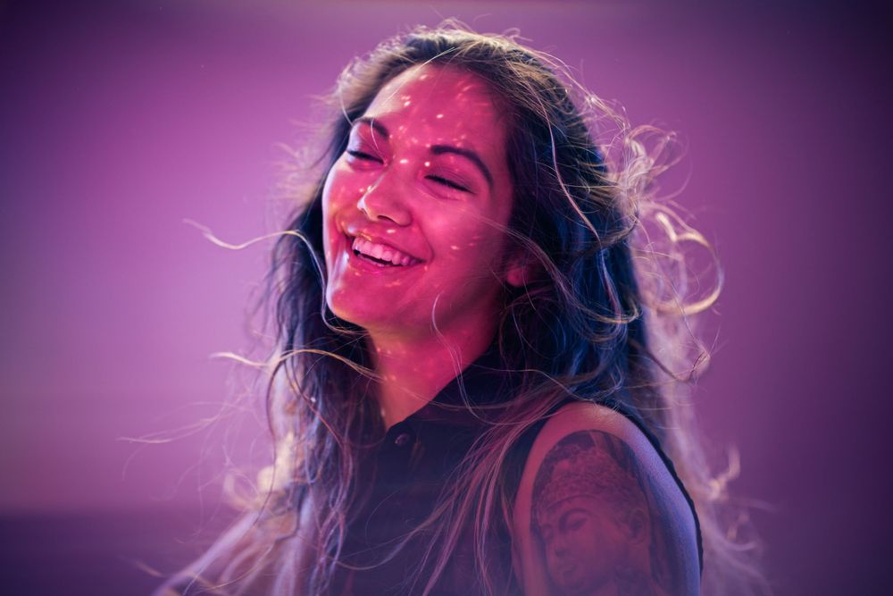 Joyful portrait with long dark hair against purple lighting showing genuine laughter.