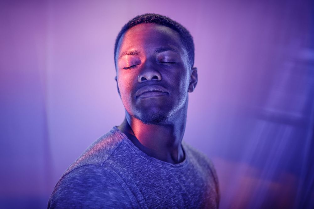 Serene portrait with purple lighting showing person with closed eyes in casual attire.